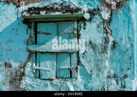 Close-up of a weathered light blue wall with a barred wooden window, reflecting the unique architectural style seen in the streets of Macau, China. Stock Photo