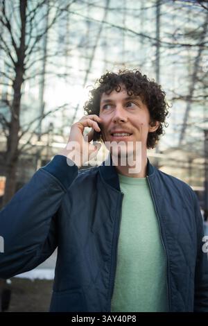 A businessman talks on a smartphone, wearing casual attire in an urban environment. The focus is on communication and connectivity, highlighting moder Stock Photo