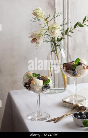 Elegant glass present a sophisticated serving of vanilla and chocolate ice cream, garnished with fresh blueberries and mint, alongside a backdrop of d Stock Photo