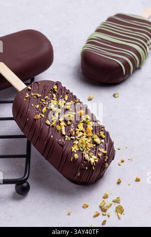 Gourmet chocolate covered ice creams garnished with matcha blend, presented elegantly on a white marble plate, adorned with chopped crushed pistachios Stock Photo