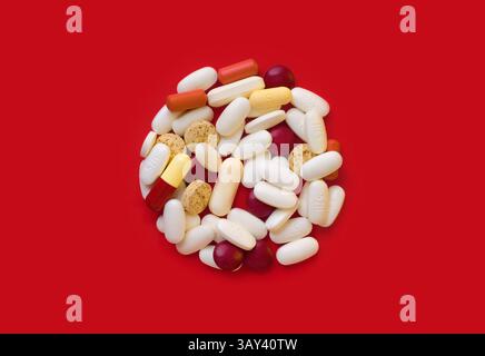 A collection of assorted medical pills in various shapes and colors, neatly arranged on a striking red backdrop, highlighting healthcare themes. Stock Photo