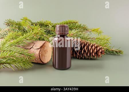 A dark brown bottle of essential oil paired with fresh pine branches, a wooden log, and a pine cone on a soft green backdrop. Stock Photo