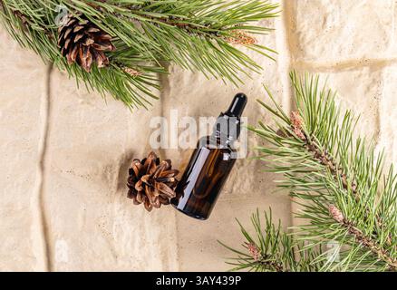Top view of a dropper bottle of essential oil surrounded by vibrant pine branches and cones on a textured background, illustrating natural coniferous Stock Photo