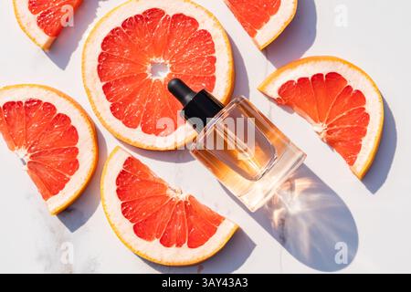 Bright grapefruit slices surround a sleek dropper bottle of essential oil for skincare on a marble surface. Sunlight illuminates a fresh, vibrant comb Stock Photo