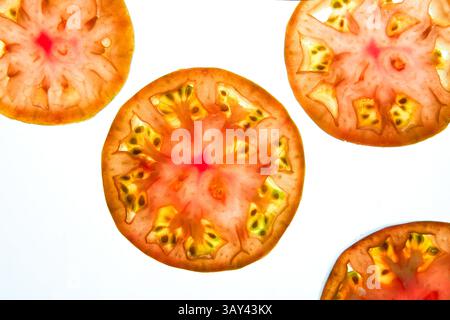 Vibrant close up image of thinly sliced tomato pieces on a light background. The slices reveal intricate patterns with shades of red, orange, and yell Stock Photo