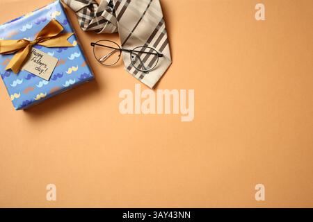 Top view of a Father's Day gift in a beautifully wrapped box alongside a stylish tie and eyeglasses, placed on a solid orange background, emphasizing Stock Photo