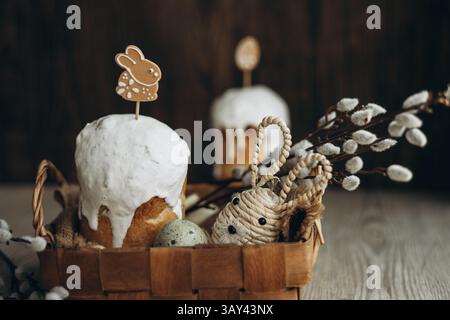 A traditional Easter setup featuring kulich, a Russian Easter bread, adorned with white icing and a bunny gingerbread cookie, alongside a basket fille Stock Photo