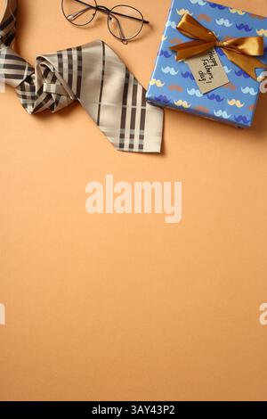 Top view of a fashionable tie, glasses, and a wrapped Father's Day gift, adorned with a bow and a tag, neatly arranged on a orange backdrop. The seren Stock Photo