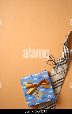 Top view of a colorful gift box with a golden bow and Happy Father's Day tag, accompanied by a stylish checkered tie and round glasses, all arranged o Stock Photo