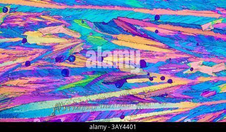 Microscopic image of Adipic acid, crystals in hues of pink, blue, yellow, and green. The image highlights the textured, abstract appearance of the cry Stock Photo