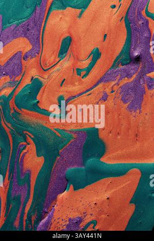 A vivid display of metallic paints in swirling patterns of orange, green, and purple, ideal for captivating backgrounds or artistic projects. Stock Photo