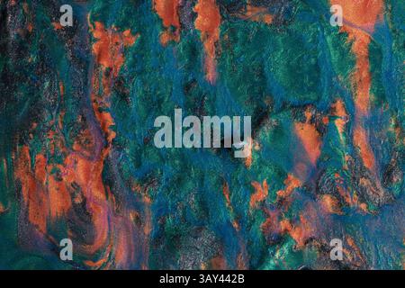 Vivid display of swirling metallic paints blending orange, blue, and green hues, creating a textured abstract background perfect for art and design. Stock Photo