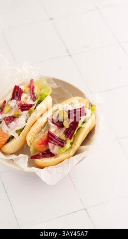 Two gourmet hot dogs of salmon topped with beet slices, lettuce, and creamy dressing. Served on a plate with a light background, highlighting the fres Stock Photo