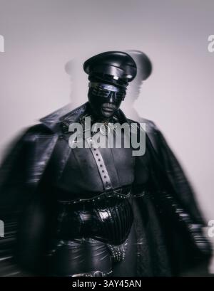 A person in black leather and futuristic accessories, including a cap and mask, stands strikingly against a blurred background, creating an edgy and a Stock Photo