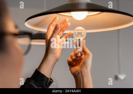 Male hands compare an incandescent light bulb and a LED lamp. Changing Light Bulb. Man installs light fixture in new home. A man changes a light bulb Stock Photo