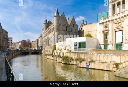 Historic stone building alongside a canal in Ghent, Belgium, reflecting on the water under a blue sky with clouds. Stock Photo