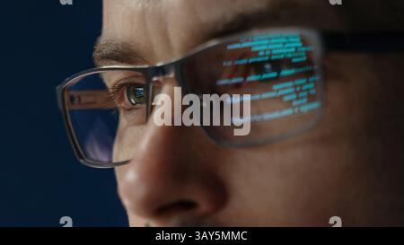 Close up of data scientist face is closely examines data. The glow of code lines reflecting in software engineer glasses and eyes. Stock Photo