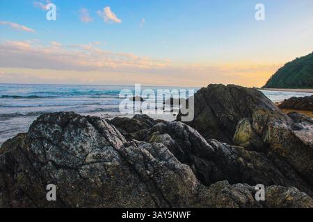 A large, imposing rock sits firmly on a picturesque beach that is located near the vast ocean, where waves gently crash against the shore Stock Photo