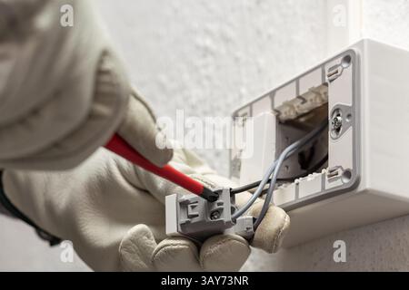 Electrician worker with screwdriver fixes electrical wires in the terminals of the diverter switch of an electrical system. Working safely with protec Stock Photo