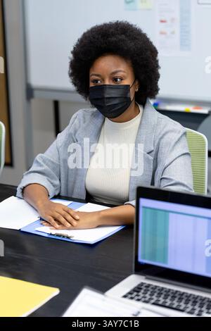 African American woman reviewing documents at table in meeting room, with clipboard and laptop Stock Photo