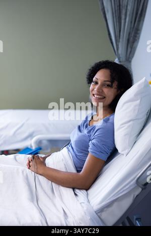 Woman reclining in bed in hospital room, using pillow and blanket, showing IV line, copy space Stock Photo