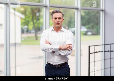 Man standing in office lobby in front of floor-to-ceiling glass windows with metal railing Stock Photo