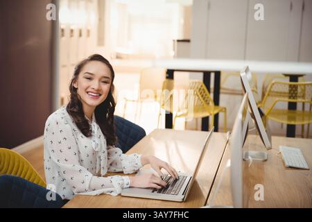 Young Asian woman typing on laptop at desk in bright office with yellow chairs, copy space Stock Photo