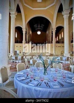 This photo captures a spacious dining hall featuring large stone arches, rustic textures, and natural light flooding through the open walls. The symme Stock Photo