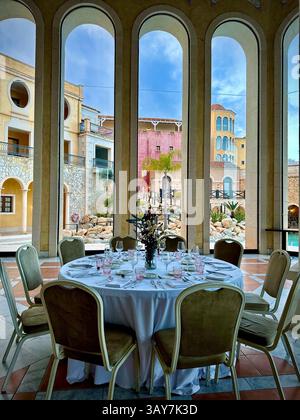 This elegant dining table is set for an upscale event, perfectly positioned within a stunning room that features large, grand windows offering a panor Stock Photo