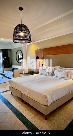 This image captures a stylish hotel room that exudes modern elegance and comfort. The spacious bedroom features a large, comfortable bed with soft, cr Stock Photo