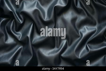 Surface features rich black eco-leather texture, highlighting deep folds and subtle reflections. This close-up reveals unique qualities of material, emphasizing its luxury and depth. Stock Photo