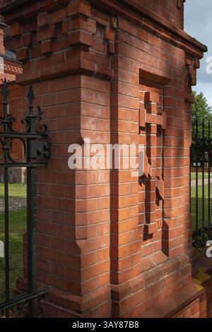 A brick wall with a cross on it. The brick wall is red and the cross is white Stock Photo