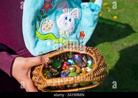 Child's hand holding basket of chocolate foil wrapped miniature Easter eggs collected on an egg hunt in Wales UK on easter day 2025  KATHY DEWITT Stock Photo