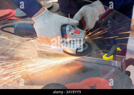 Mechanic using angle grinder and working with metal in workshop. Industry Stock Photo