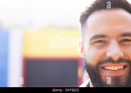Young man smiling broadly in front of colorful painted mural outdoors, enjoying sunny mood Stock Photo