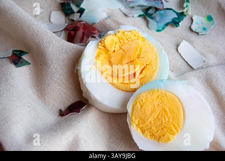 Two hard-boiled eggs placed on a plain background, surrounded by fragments of colorful cracked shells. Stock Photo
