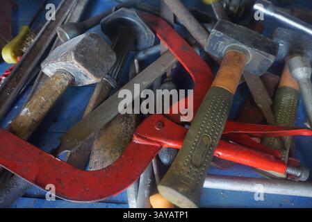 Various tools such as hammers, large safety pliers, a sheet metal cutter, files, a cross for wheel bolts and a wire brush scattered randomly Stock Photo