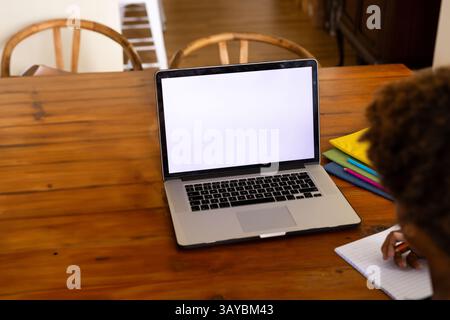 African American person writing in notebook on wooden dining table at home, with laptop and folders Stock Photo