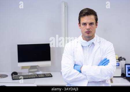young man standing with arms crossed in lab office, with computer monitor and keyboard, copy space Stock Photo