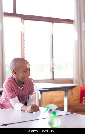 African American boy sitting at classroom desk interacting with model wind turbine and spray bottle Stock Photo