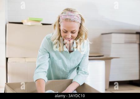 Woman kneeling at home packing bubble wrap into open cardboard box with books and boxes Stock Photo