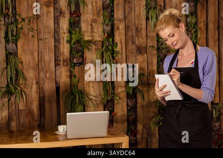 Young adult woman writing in spiral-bound notepad in cafe, with laptop, coffee cup, copy space Stock Photo