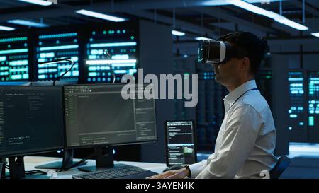 Admin in data center using virtual reality tech to ensure system can handle networking tasks. Server room worker wearing VR headset to track network traffic with PC, making improvements, camera A Stock Photo