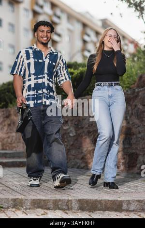 Happy Young Couple Walking Hand in Hand Outdoors in Urban Setting Stock Photo