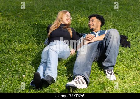 Young Couple Lying on Grass Smiling at Each Other in Urban Park Stock Photo