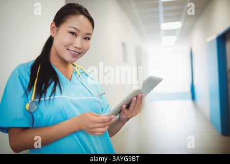 Asian woman nurse standing in hospital corridor holding tablet and wearing stethoscope, copy space Stock Photo