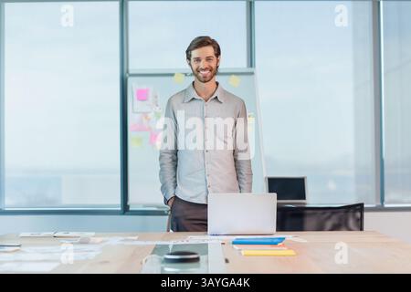 Man standing behind meeting table in modern office, showing flip chart and laptop, copy space Stock Photo