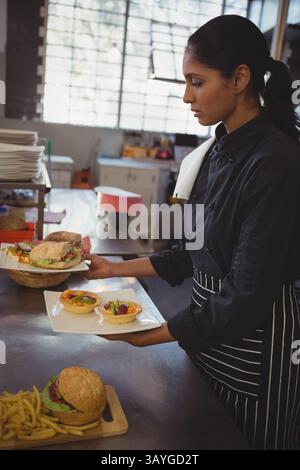 Indian woman chef plating tartlets and sandwiches on white plate in restaurant kitchen, copy space Stock Photo