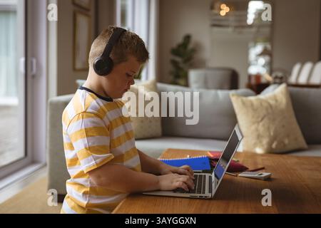 child typing on laptop in living room near dining area, with headphones and notebooks, copy space Stock Photo