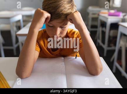 Schoolboy sitting at desk in classroom, focusing on open notebook and yellow ruler Stock Photo